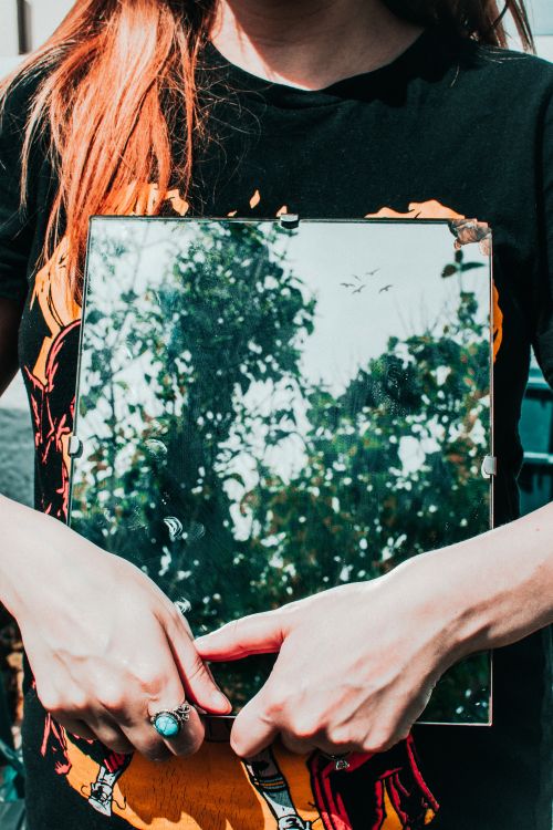 Free A person holding a mirror reflecting trees and sky outdoors. Stock Photo