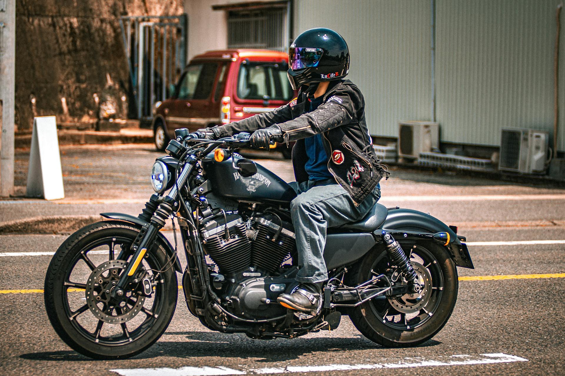 A biker in helmet rides a Harley Davidson motorcycle on a city street during the day.