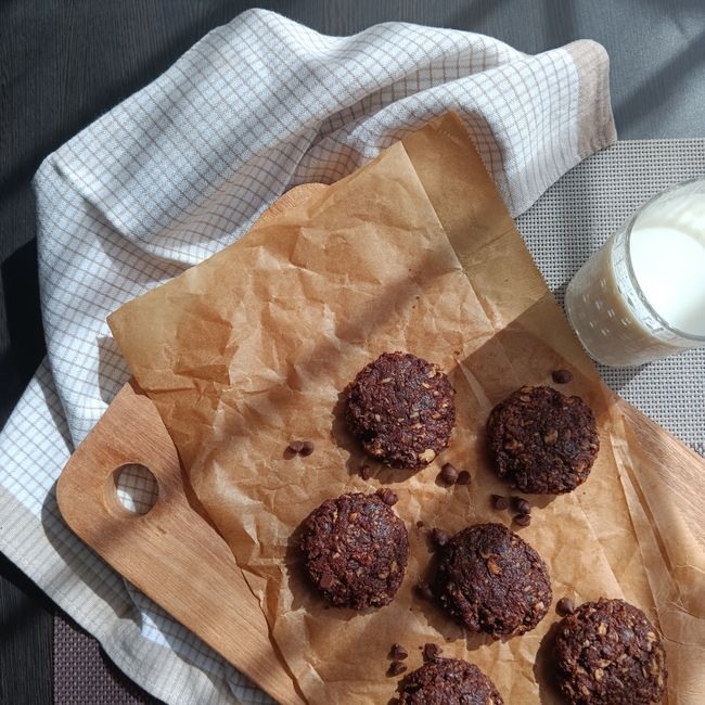 A stack of glossy, fudgy no-bake chocolate oatmeal cookies studded with oats, cooling on a sheet of wax paper.