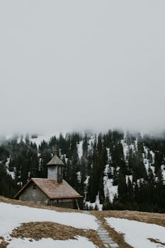 A quaint chapel amidst foggy snow-covered mountains in Le Grand-Bornand, France.