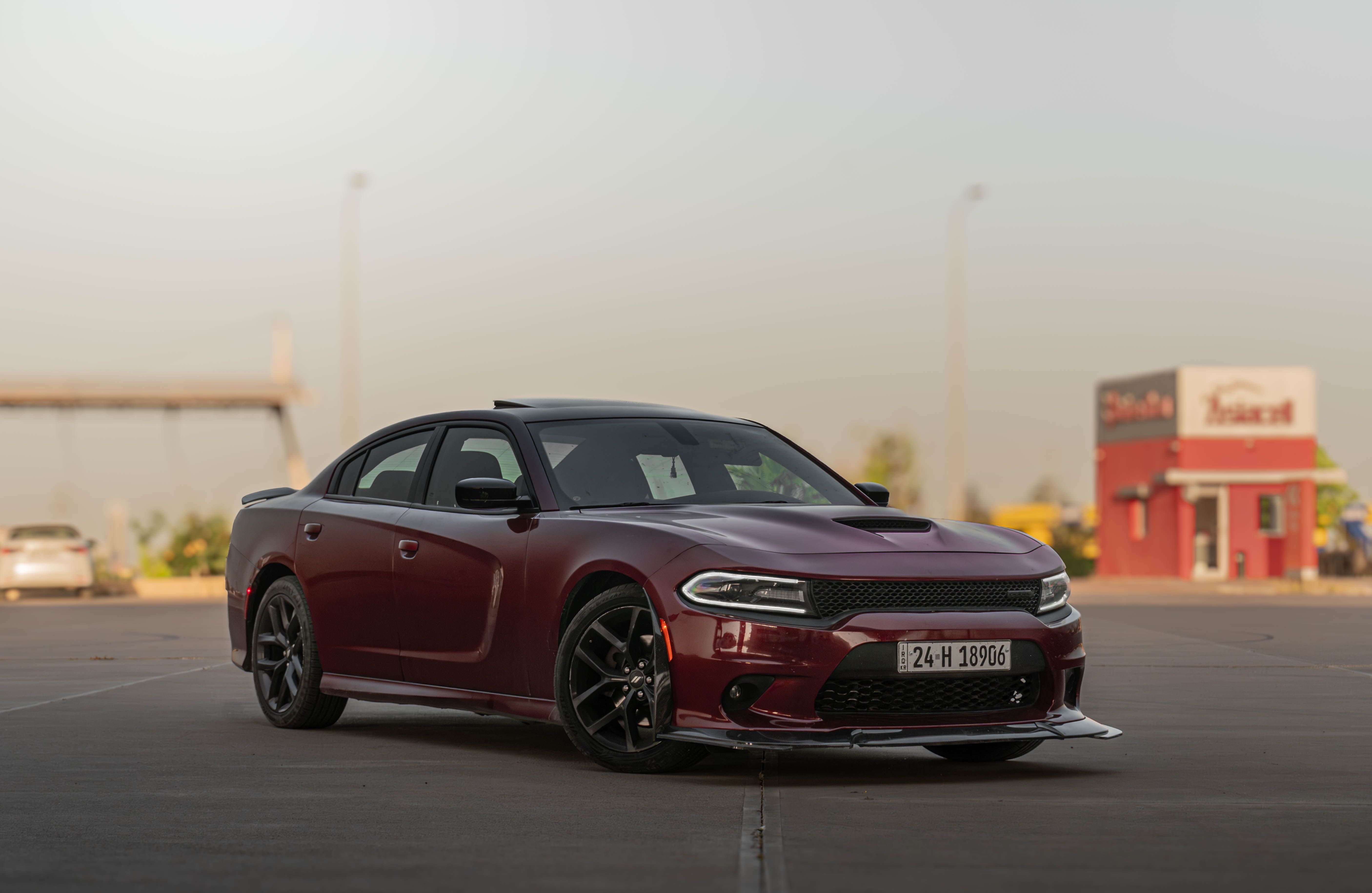 A sleek dark red Dodge Charger sports car parked in an urban area with a clear sky.