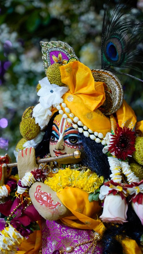 Free Colorful statue of Hindu deity playing flute adorned with flowers and ornaments. Stock Photo