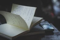 在光线昏暗的室内，打开木桌上手机旁那本带有手写笔记的笔记本