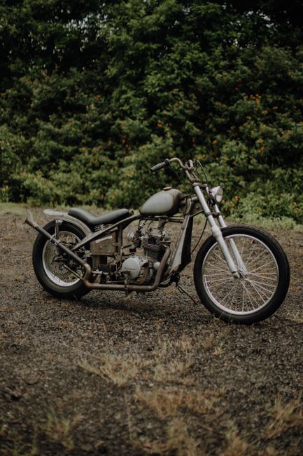 A classic vintage motorcycle parked on a gravel road with lush greenery in Jakarta, Indonesia.