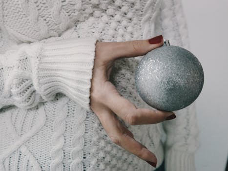 特写镜头中，一名妇女手持闪闪发光的圣诞球，身穿舒适的针织衫