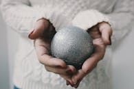 特写镜头中，一位女性在舒适的环境里双手握着一件闪闪发光的银色圣诞装饰品