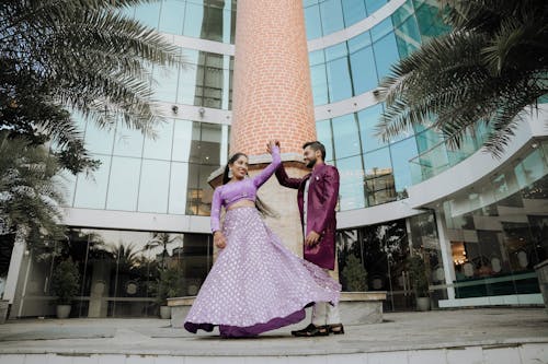 A couple in purple dress pose for a photo in front of a building