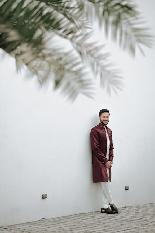 A man in a maroon sherwani leaning against a wall
