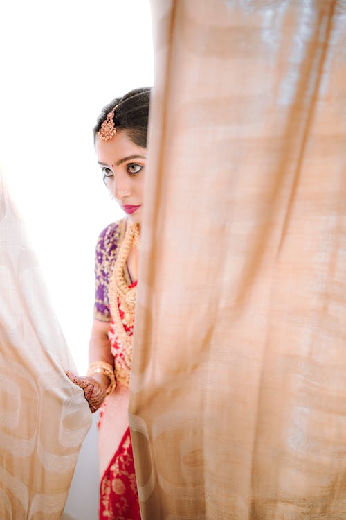 A woman in a traditional indian wedding dress looking out of a window