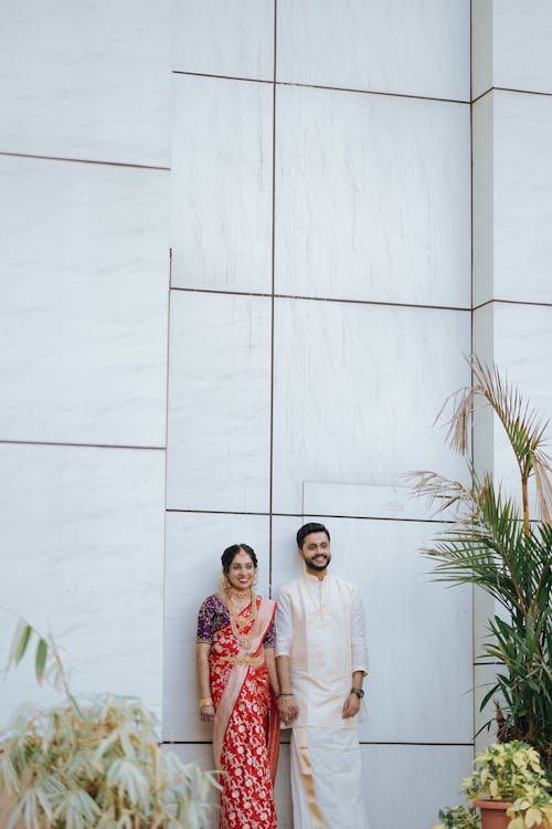 A couple in traditional attire standing in front of a white wall