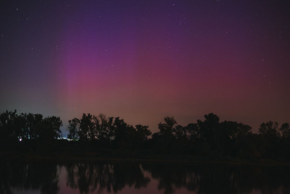 Beautiful view of an aurora borealis over a peaceful lake with silhouetted trees at night.