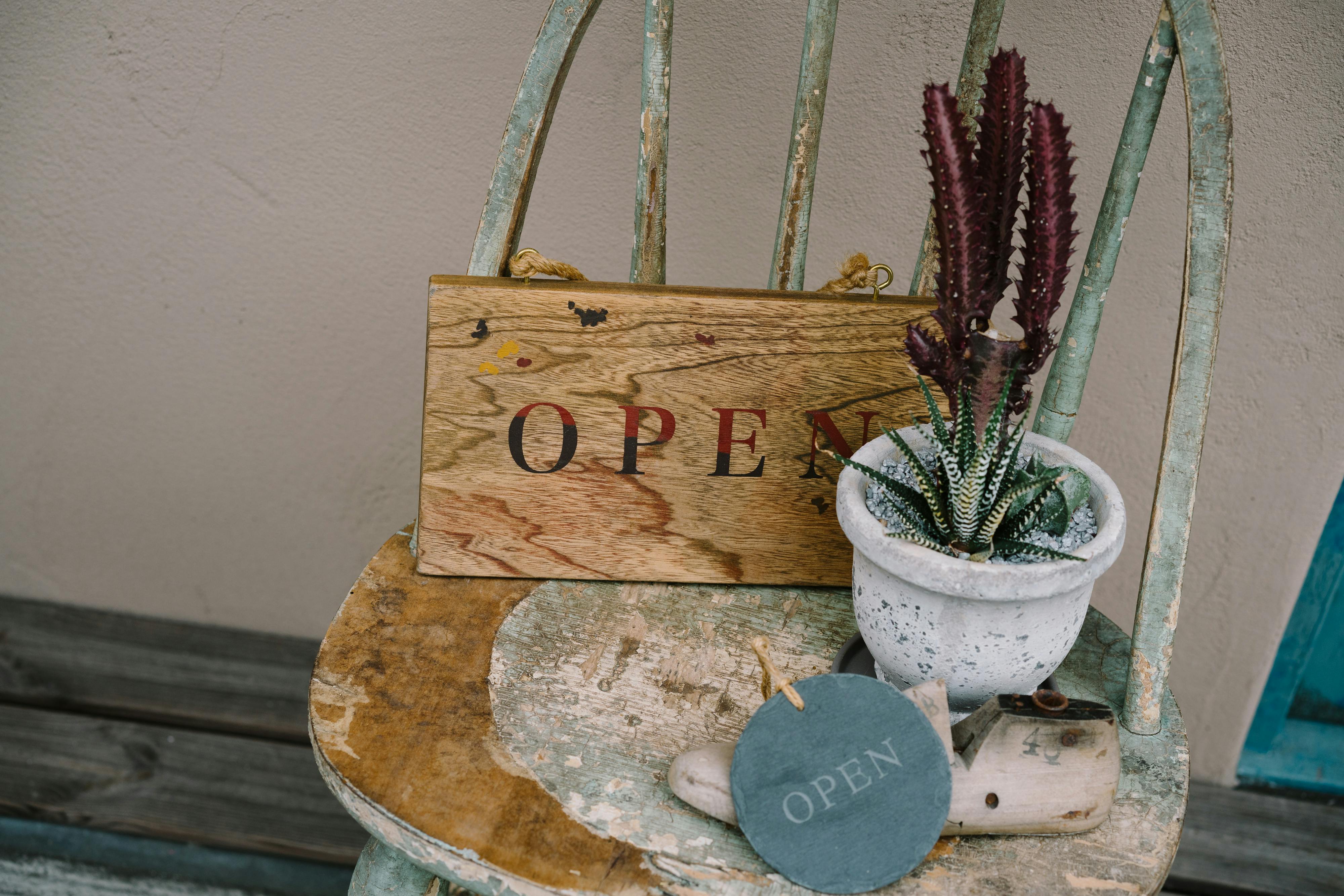 A vintage chair with an open sign, potted cactus, and rustic decor, creating a welcoming atmosphere.
