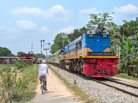 Cyclist follows train along sunny rural railway track, capturing contrast of old paths and modern transit.