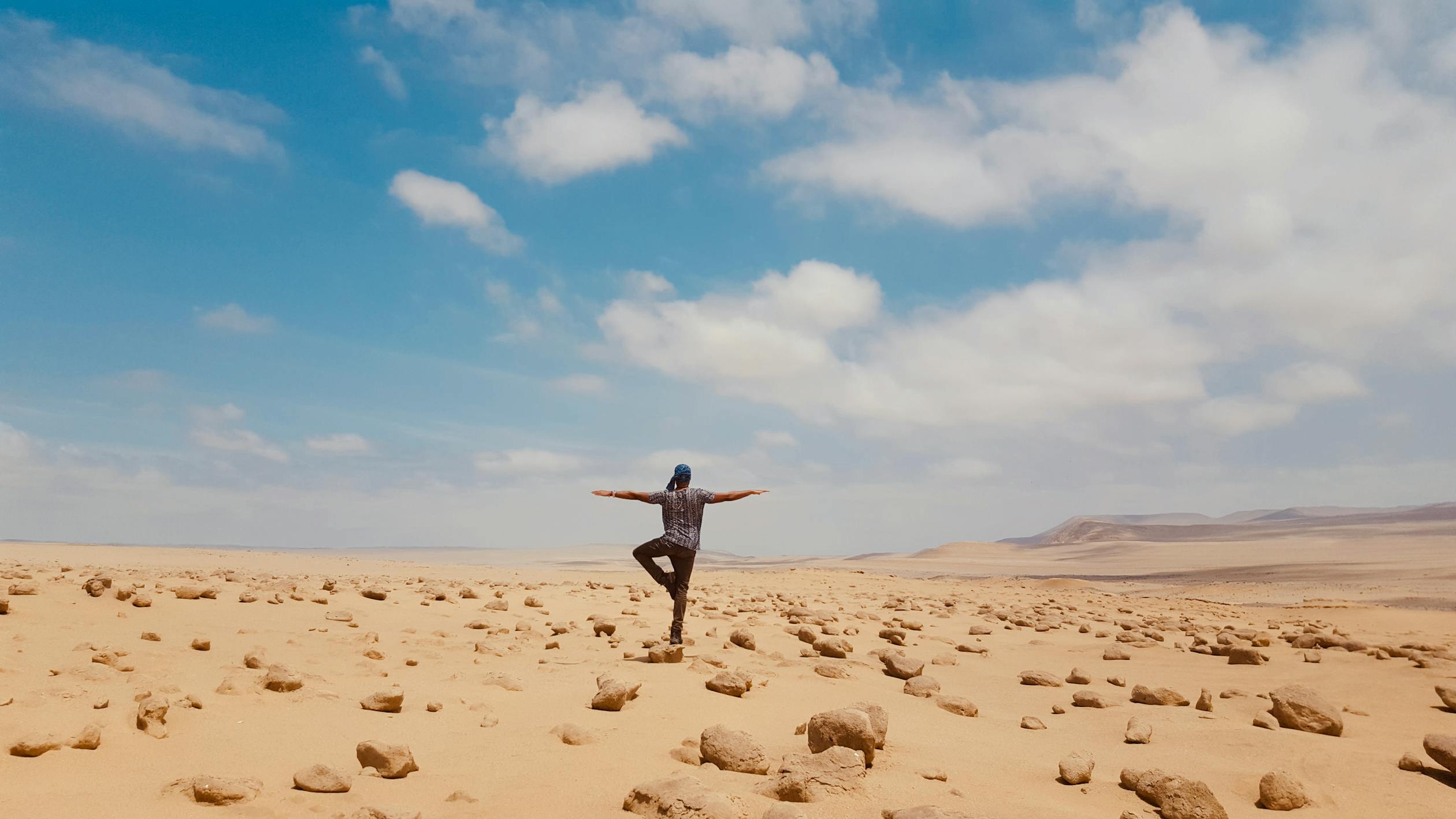 free photo of man standing on one leg in a desert