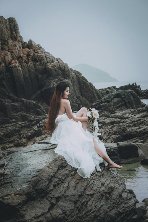 A bride sitting on rocks in a wedding dress
