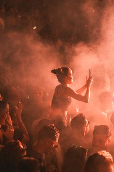 Excited crowd at a nighttime concert surrounded by colorful smoke and music energy.