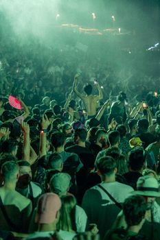 A vibrant crowd enjoying a nighttime outdoor music festival with lights and smoke effects.