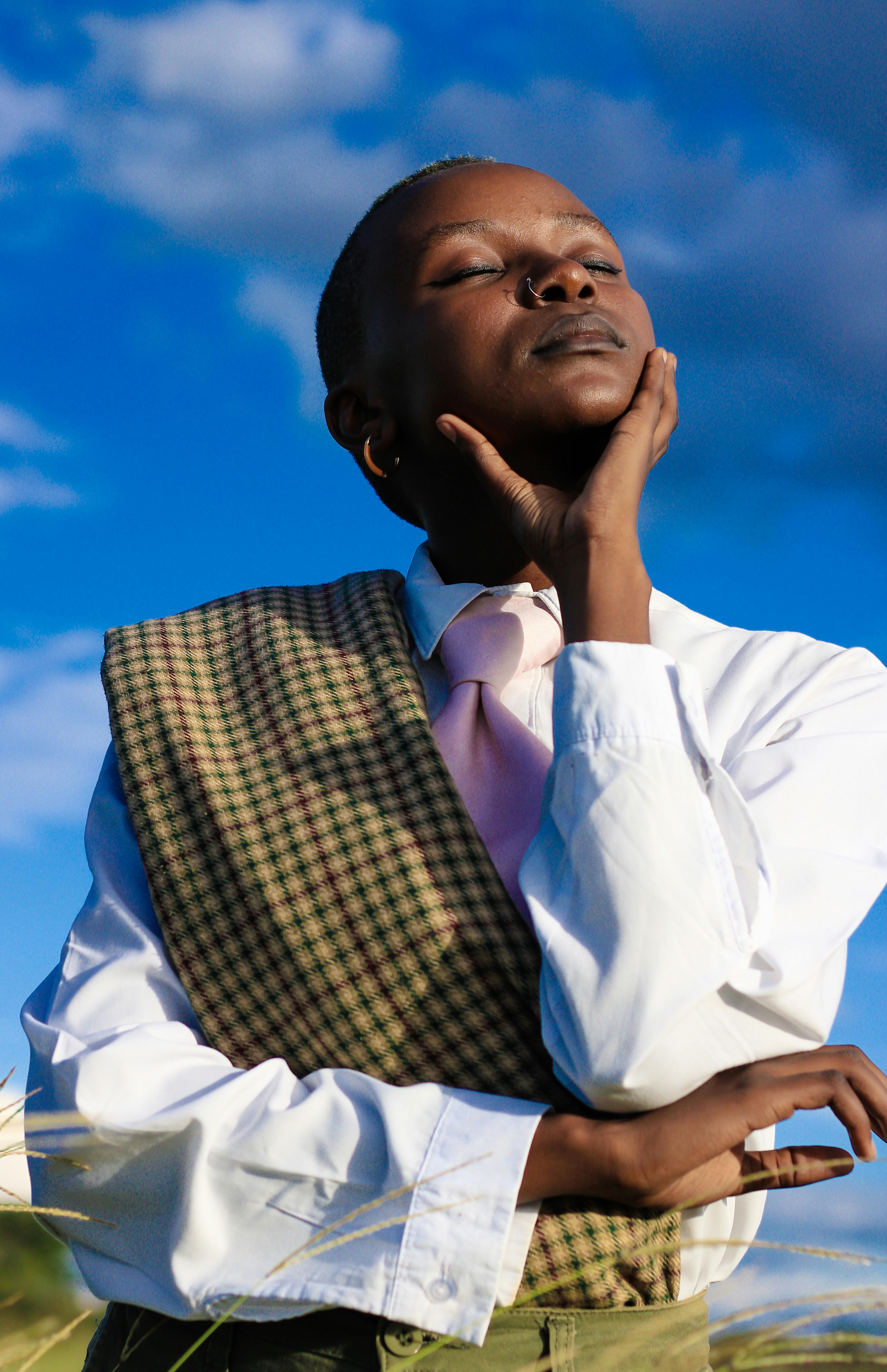 Elegant portrait of an African woman standing outdoors with eyes closed under a blue sky.