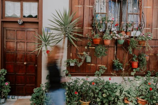 A blurred motion shot of a woman walking by a charming wooden doorway adorned with lush potted plants.
