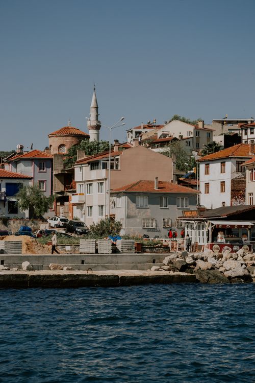Free Picturesque coastal town featuring traditional houses and a minaret against a summer sky. Stock Photo