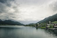 在多云的天空下，群山环绕着宁静的湖泊，奥地利村庄的风景显得格外美丽