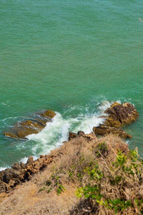 Free Stunning view of Vũng Tàu's rocky shoreline with turquoise waves crashing against the coast. Stock Photo