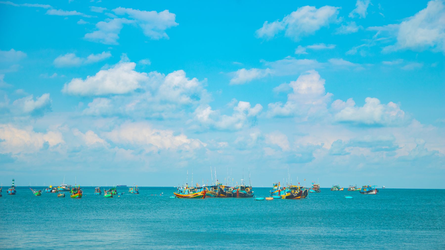 Vibrant long-tail boats on a turquoise sea under a bright blue sky in Vũng Tàu, Vietnam.