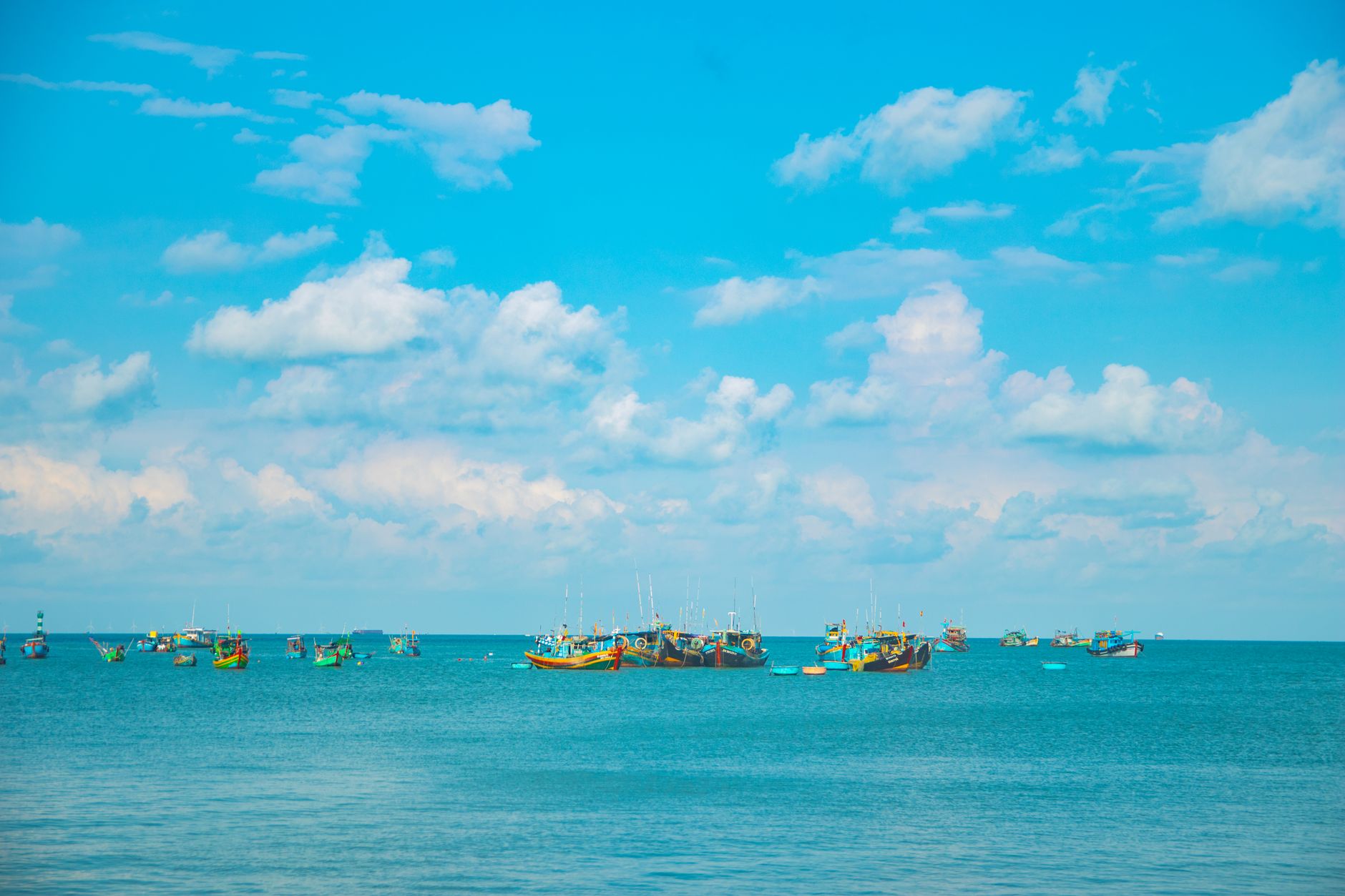 Vibrant long-tail boats on a turquoise sea under a bright blue sky in Vũng Tàu, Vietnam.