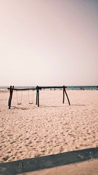 A quiet beach scene with an empty swing set on the sandy shore under clear skies.