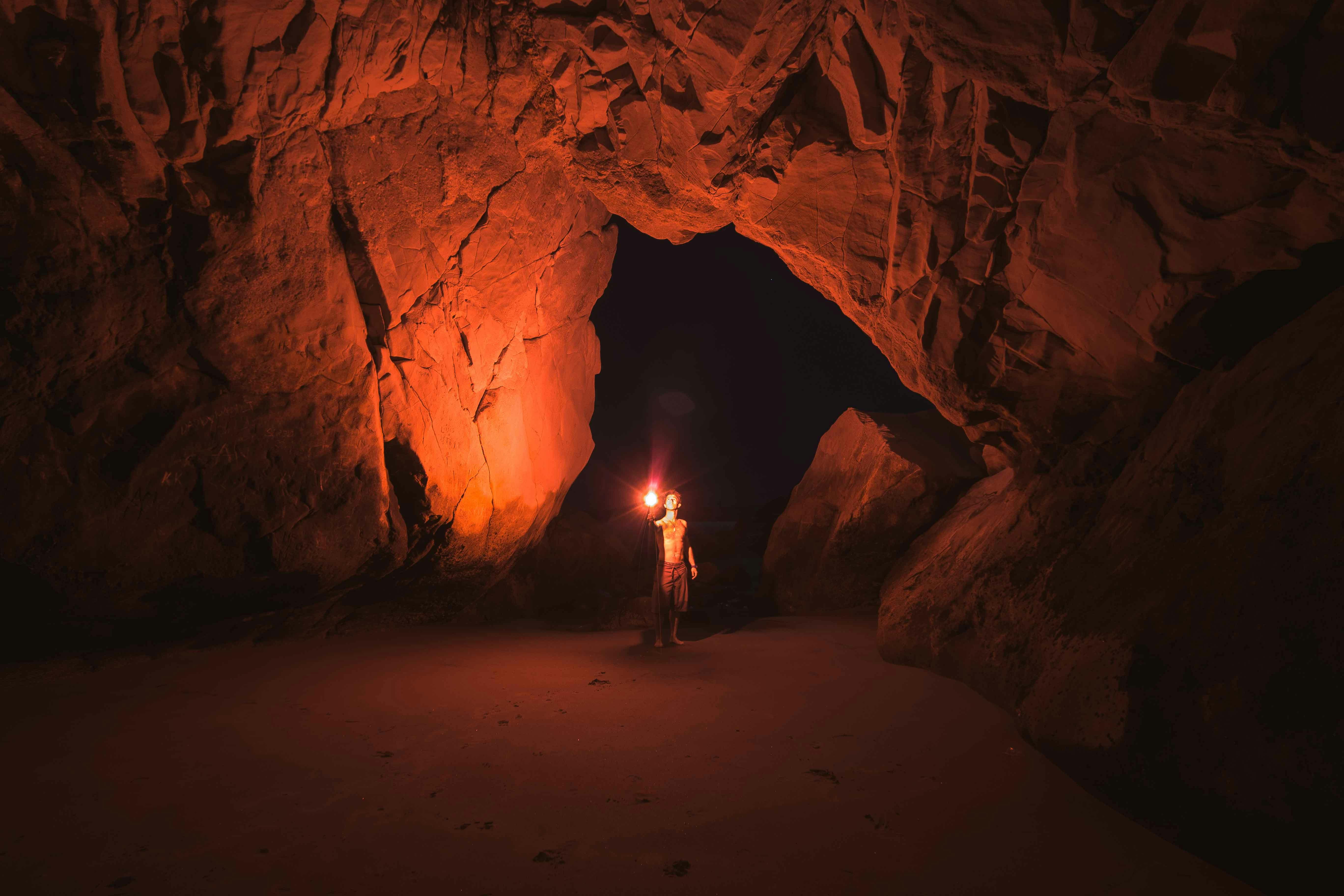 person standing and holding lamp inside cave