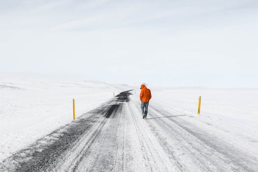 A person in a red jacket walking alone on an icy road in Iceland's winter landscape.