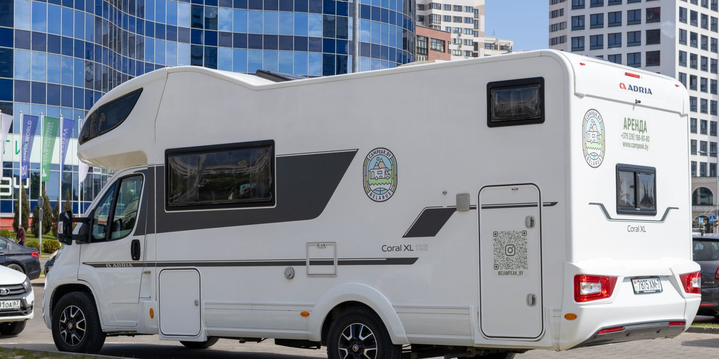 A glossy white Class C motorhome parked beside glass office buildings