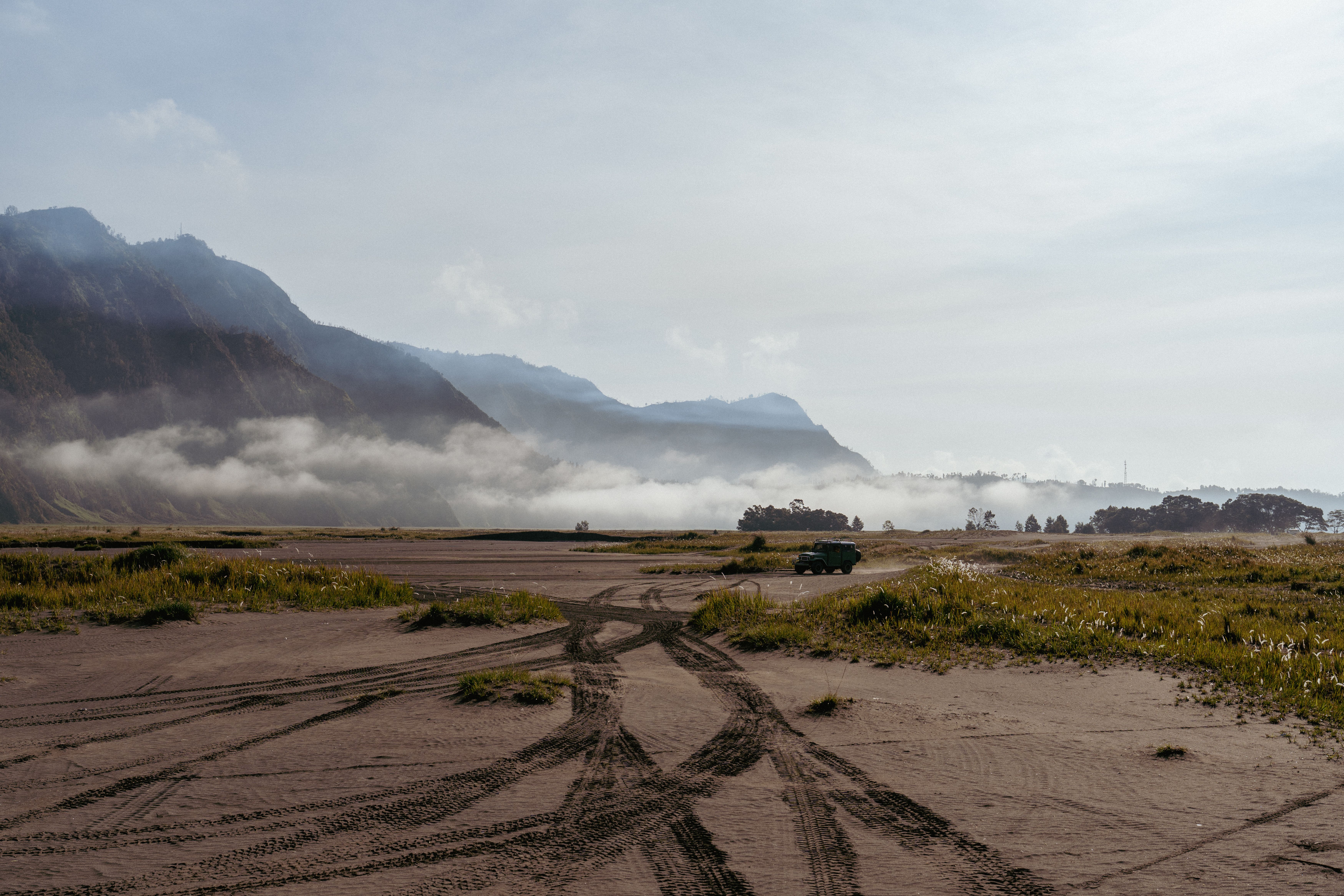 Offroad vehicle in a vast mountainous landscape with clouds and tire tracks, perfect for adventure themes.