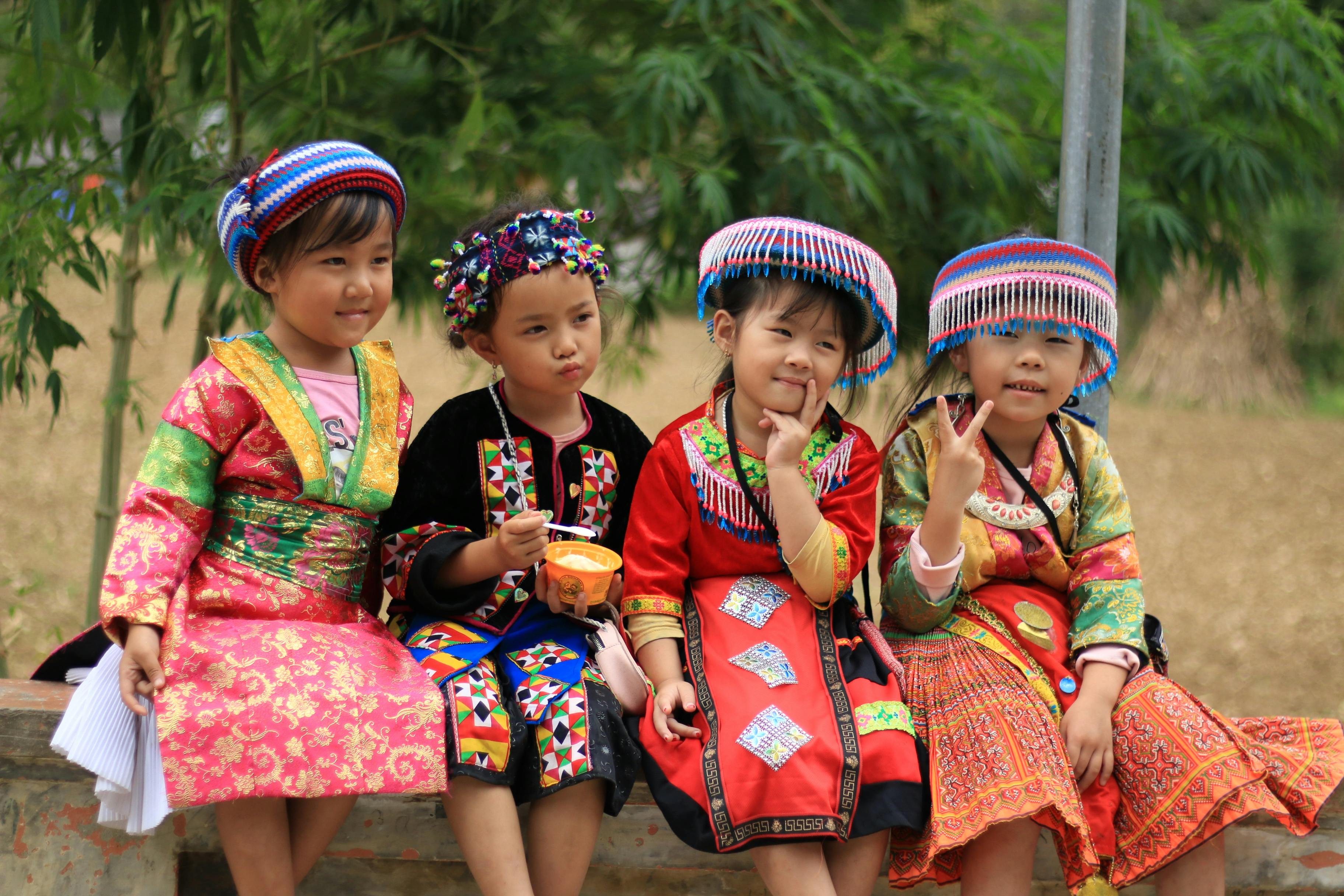 Group of Vietnamese children in traditional colorful costumes, sitting outdoors.