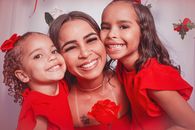 A heartwarming portrait of a mother with her two daughters in matching red dresses, smiling joyfully.