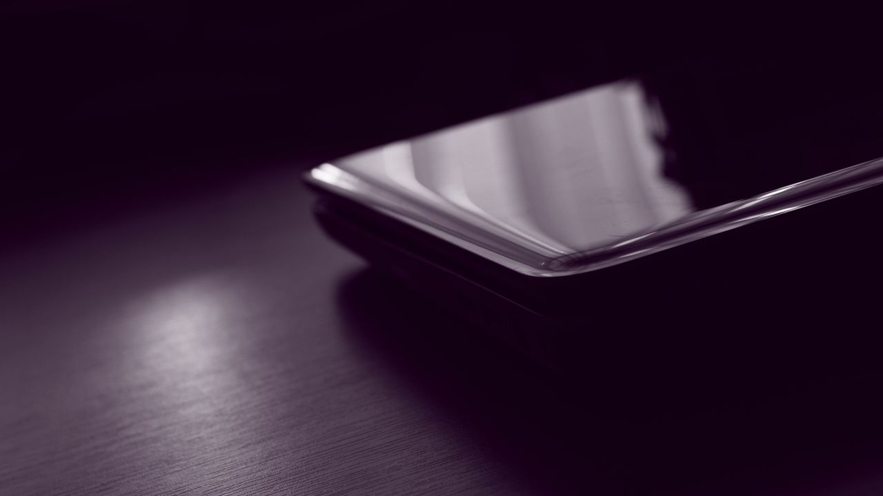a dark minimalist close up of a smartphone reflecting light on a surfa