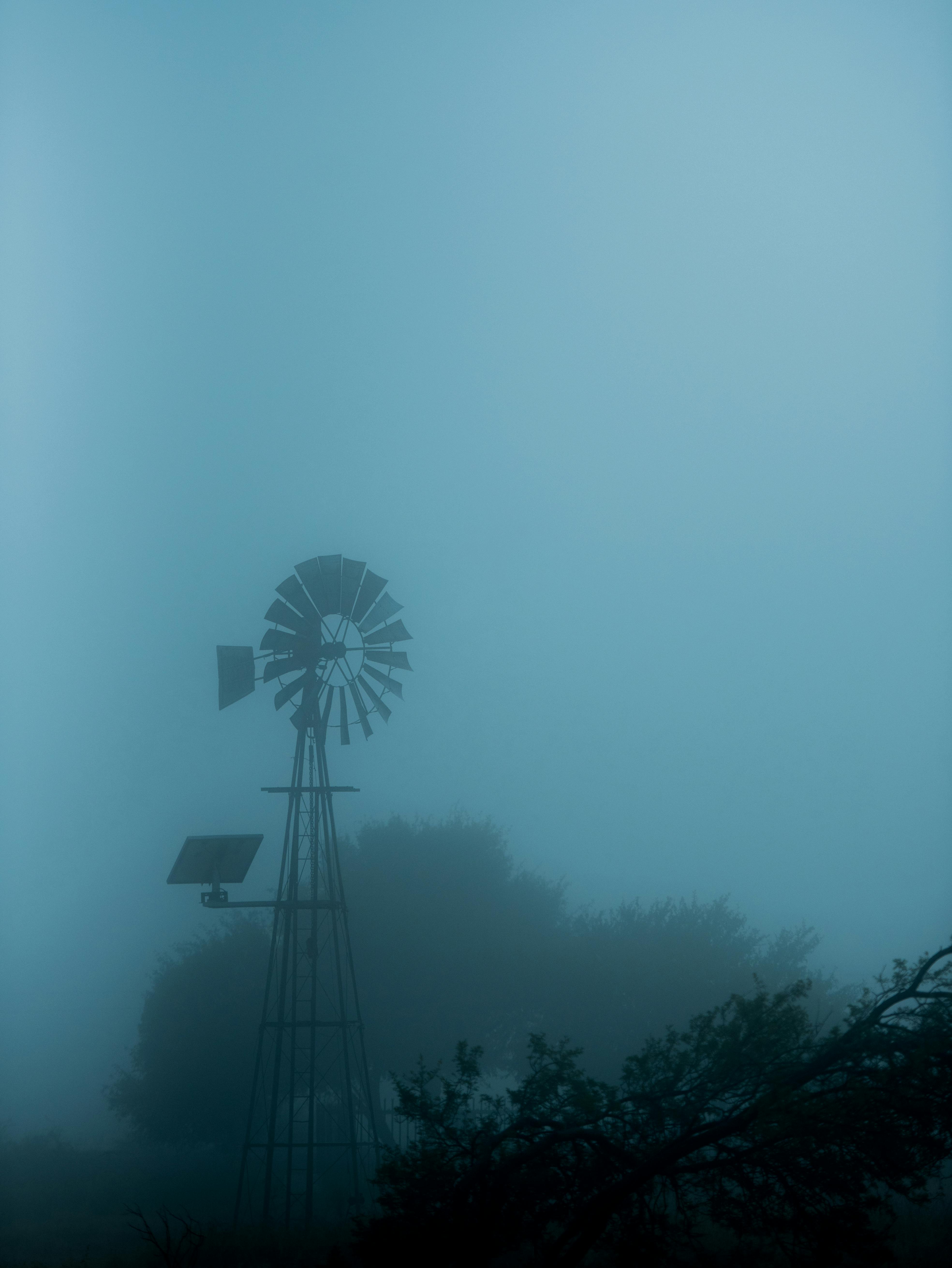 Eerie foggy scene with silhouette of windmill in rural landscape, creating a mystic atmosphere.