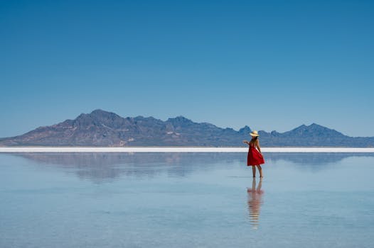 A woman in a red dress poses at a scenic salt flat with mountains in the background, capturing the serene beauty of summer outdoors.