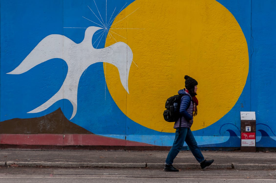 A man walking past a mural depicting a dove and a sun