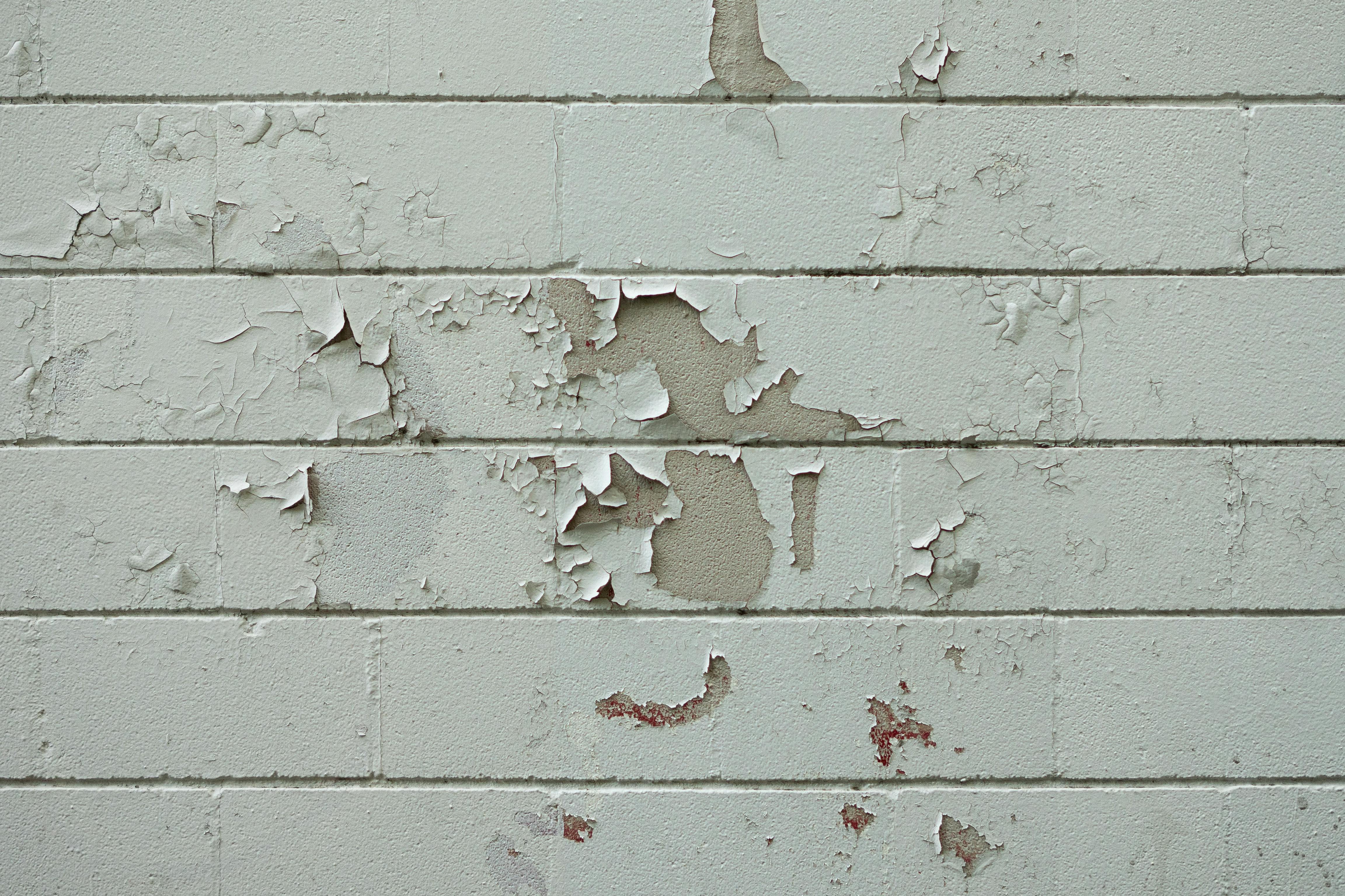 Free Close-up of an old brick wall with peeling white paint, showcasing urban decay and texture. Stock Photo