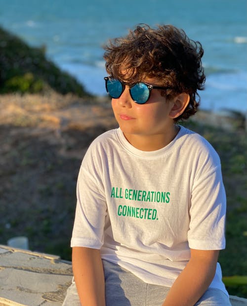 A boy wearing sunglasses sitting on a bench