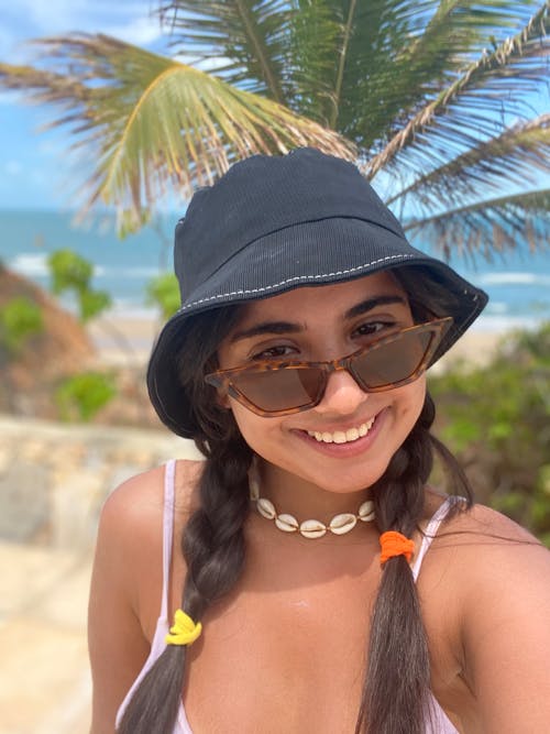 A woman wearing a hat and sunglasses smiling at the camera