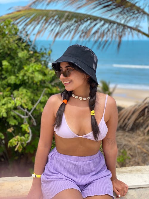 A woman in purple shorts and a hat sitting on a beach