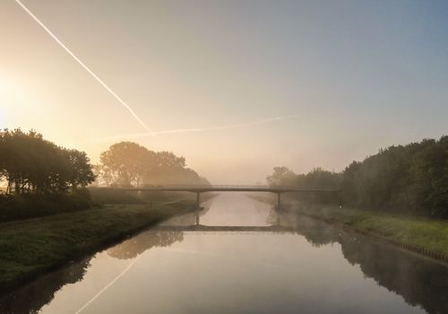 Free Serene countryside scene with mist over a river and bridge during sunrise in De Wijk, Netherlands. Stock Photo
