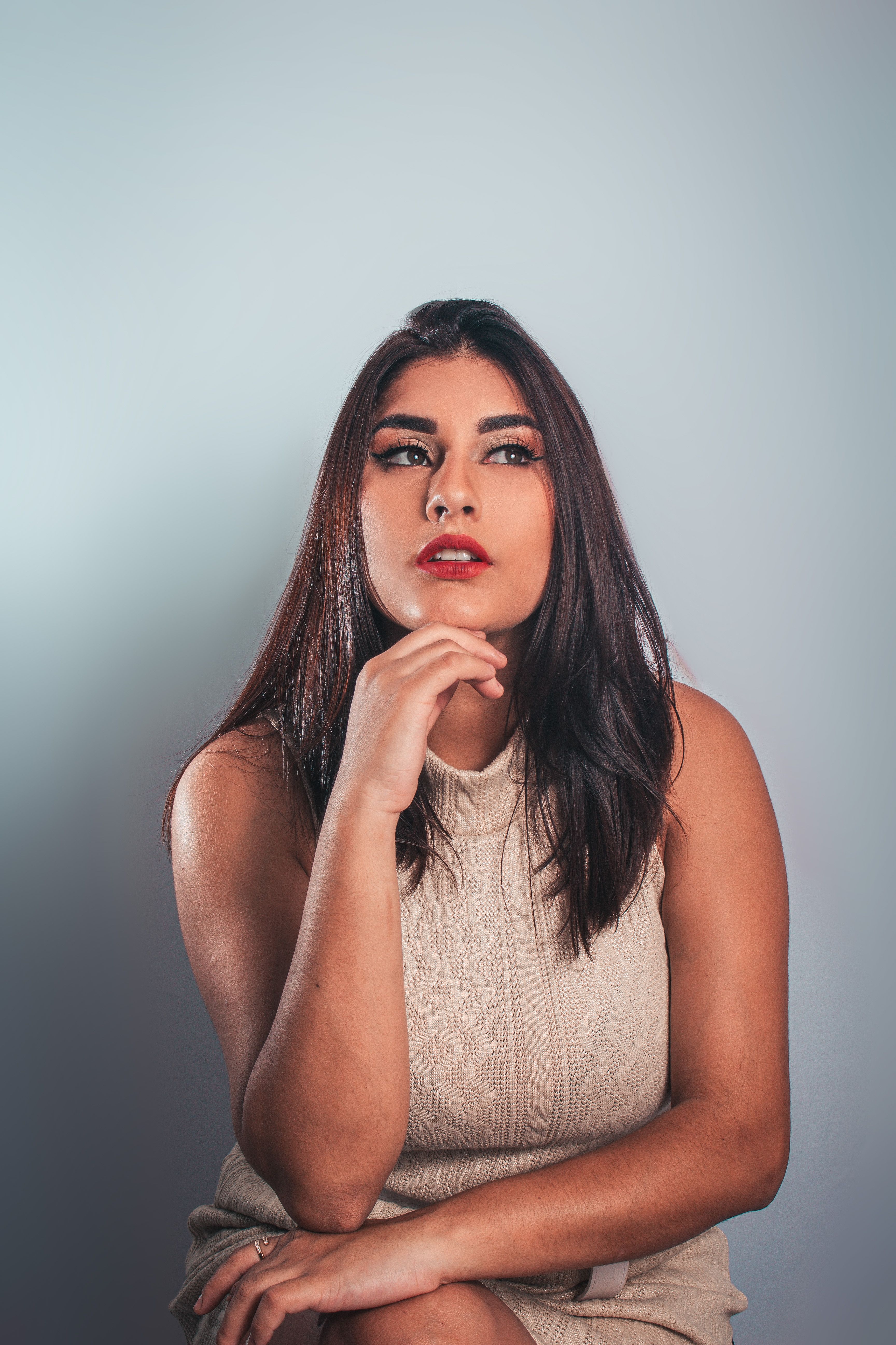 Brunette Woman in Beige Dress Sitting with Hand on Chin · Free Stock Photo
