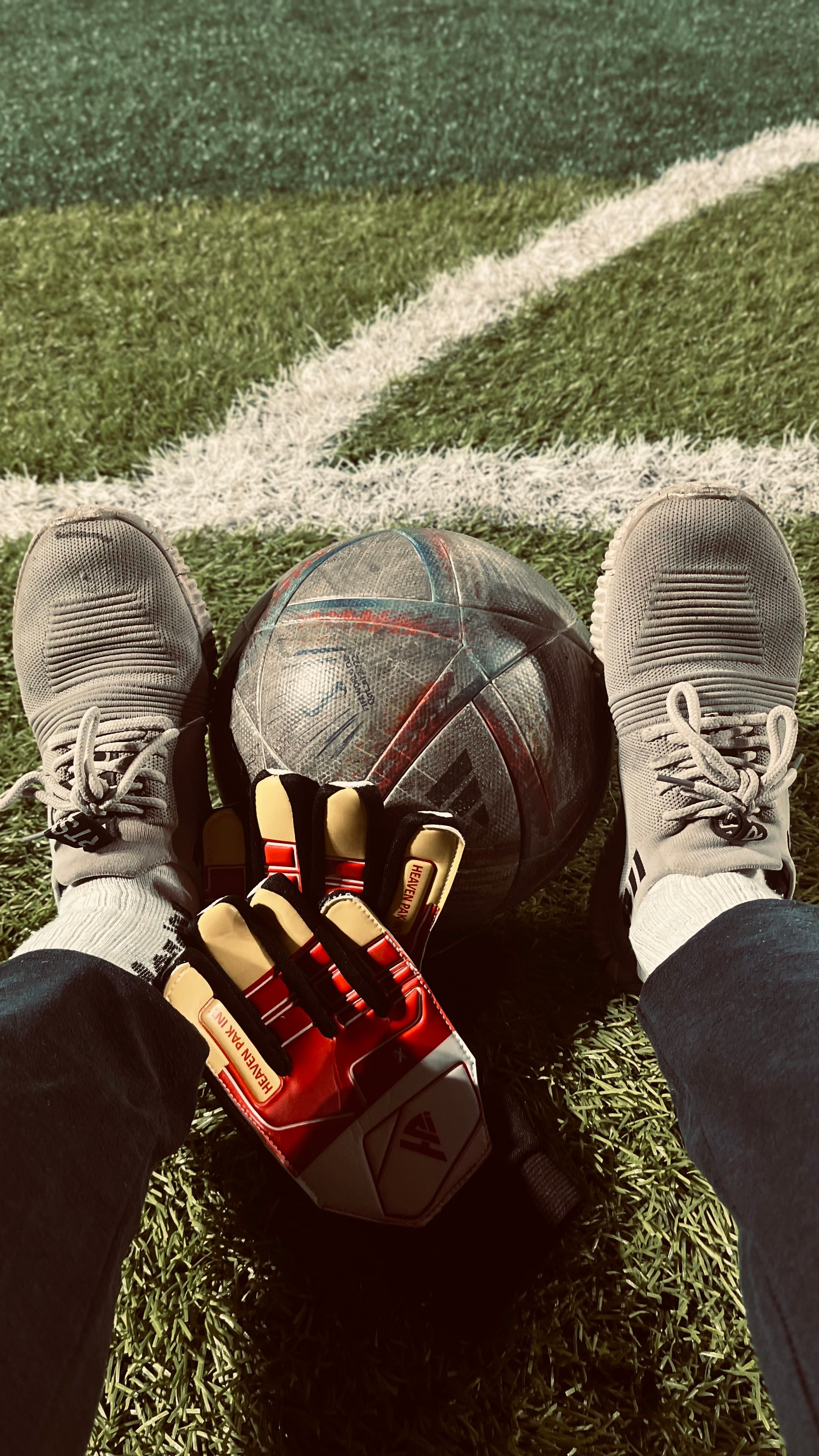 View from a goalkeeper's perspective with gloves, soccer ball, and shoes on a pitch.