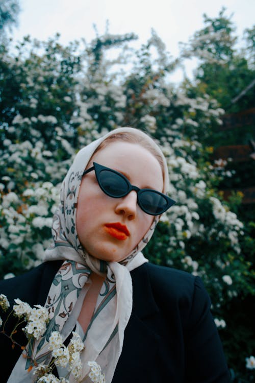A woman with sunglasses and a scarf is posing