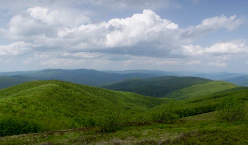 A view of a green hill with some clouds