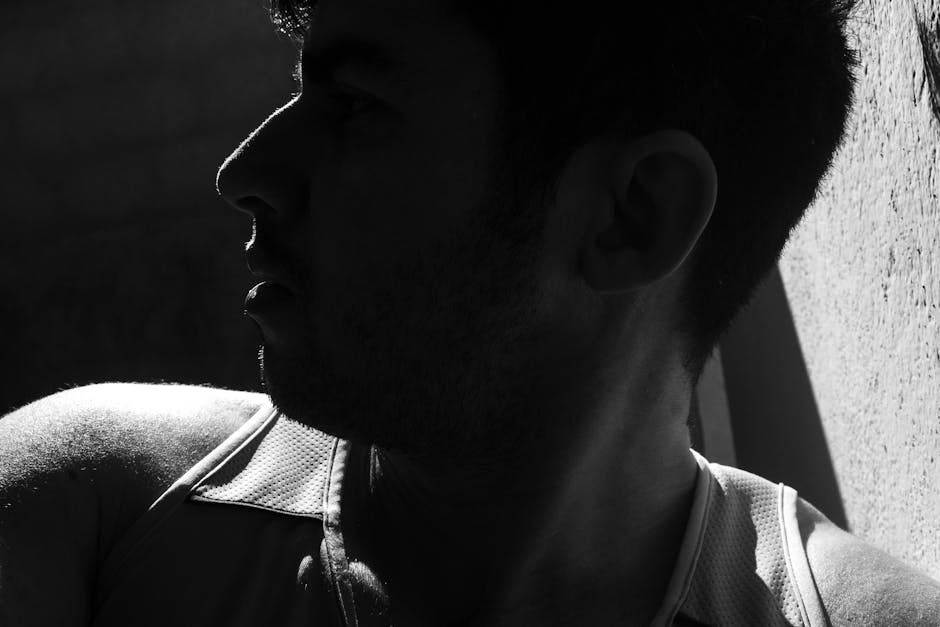 A striking black and white side silhouette of a young man in a vest with high contrast lighting.