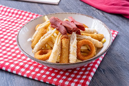 A plate of fries and onion rings on a red and white checkered tablecloth
